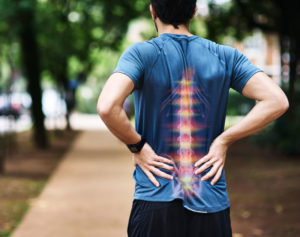 Image of a male athelete holding his back with two hands and feeling pain in standing position from backside